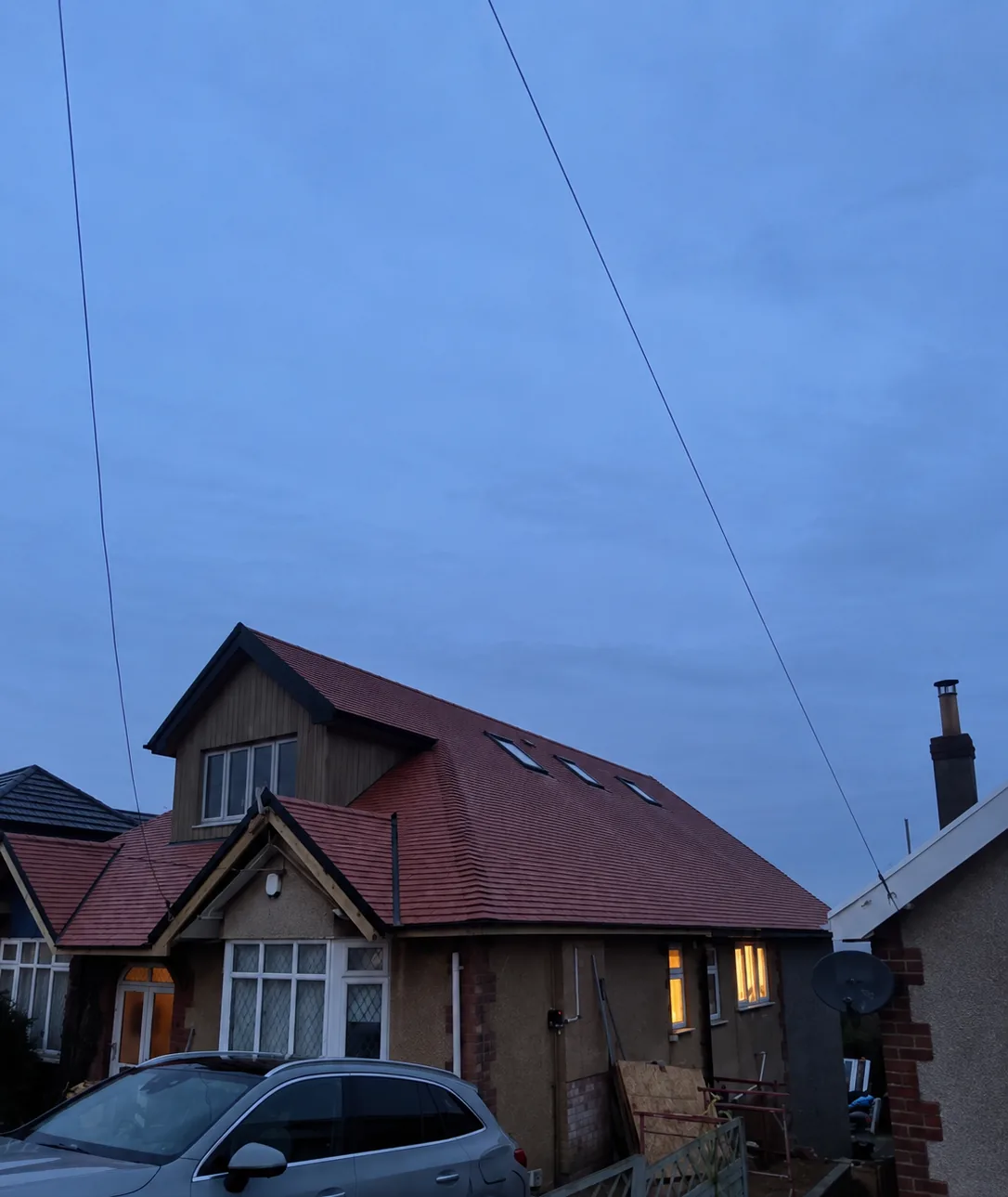 A timber-clad dormer, three rooflights and a newly tiled red roof on a converted bungalow, photographed at dusk with lights on inside