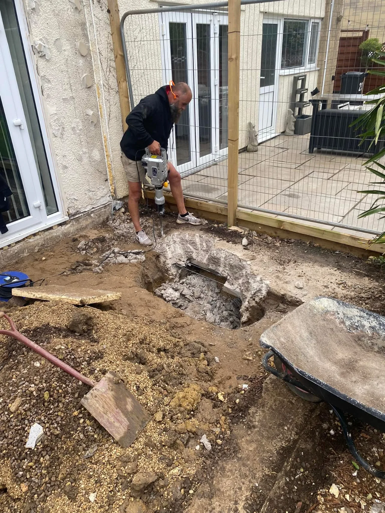 Breaking out concrete with a breaker for new footings beside a house, behind site fencing